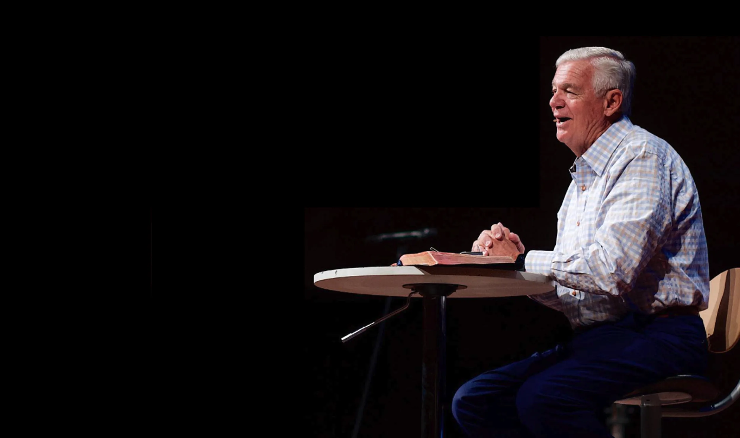 Pastor Ken Whitten seated at a table with his Bible, teaching